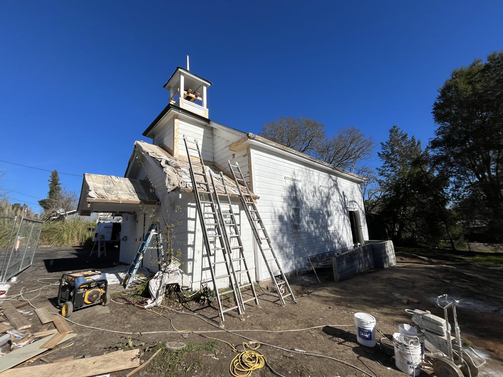 Small white church building with ladders up for exterior prep and painting
